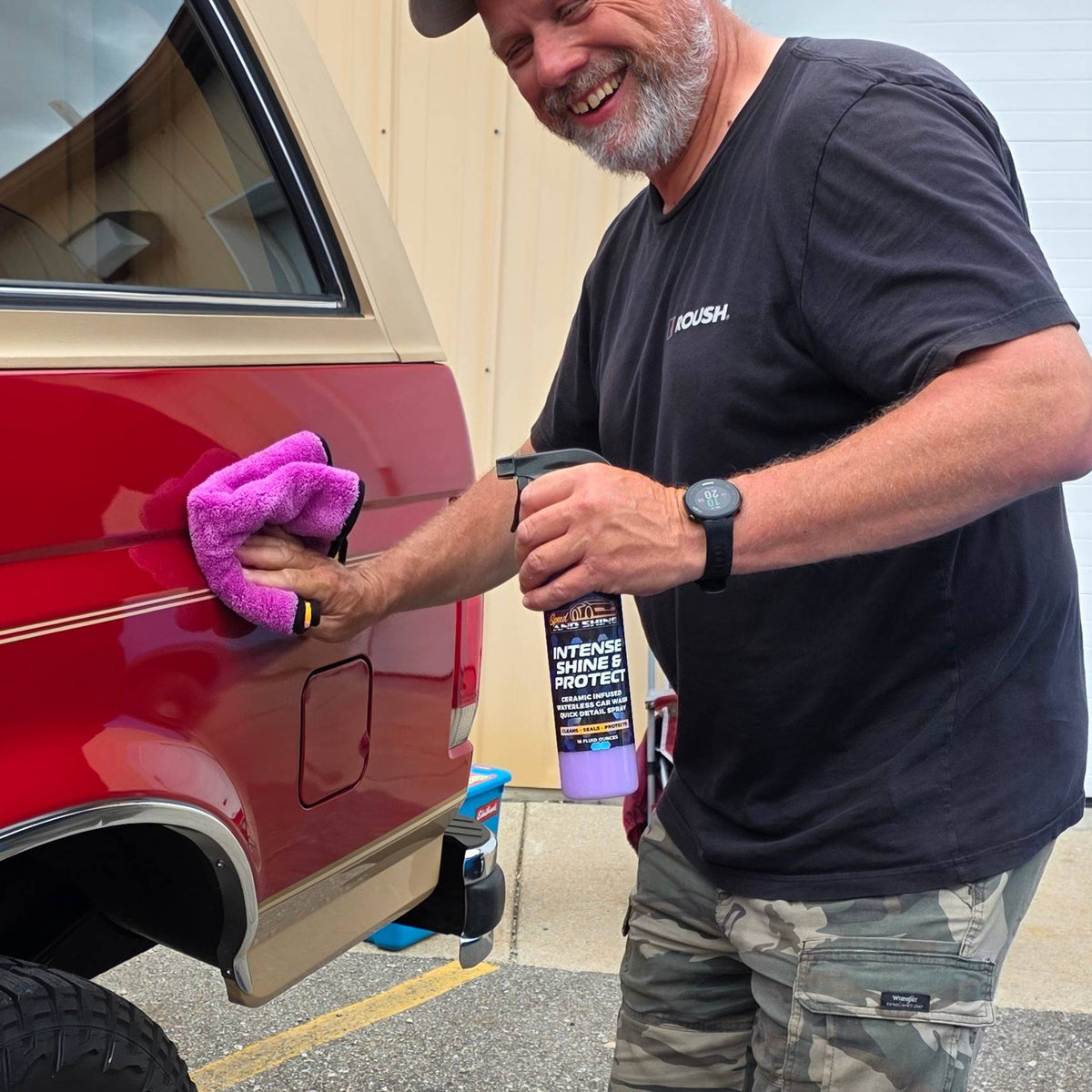A man is cleaning the side door of a red truck with a purple microfiber cloth