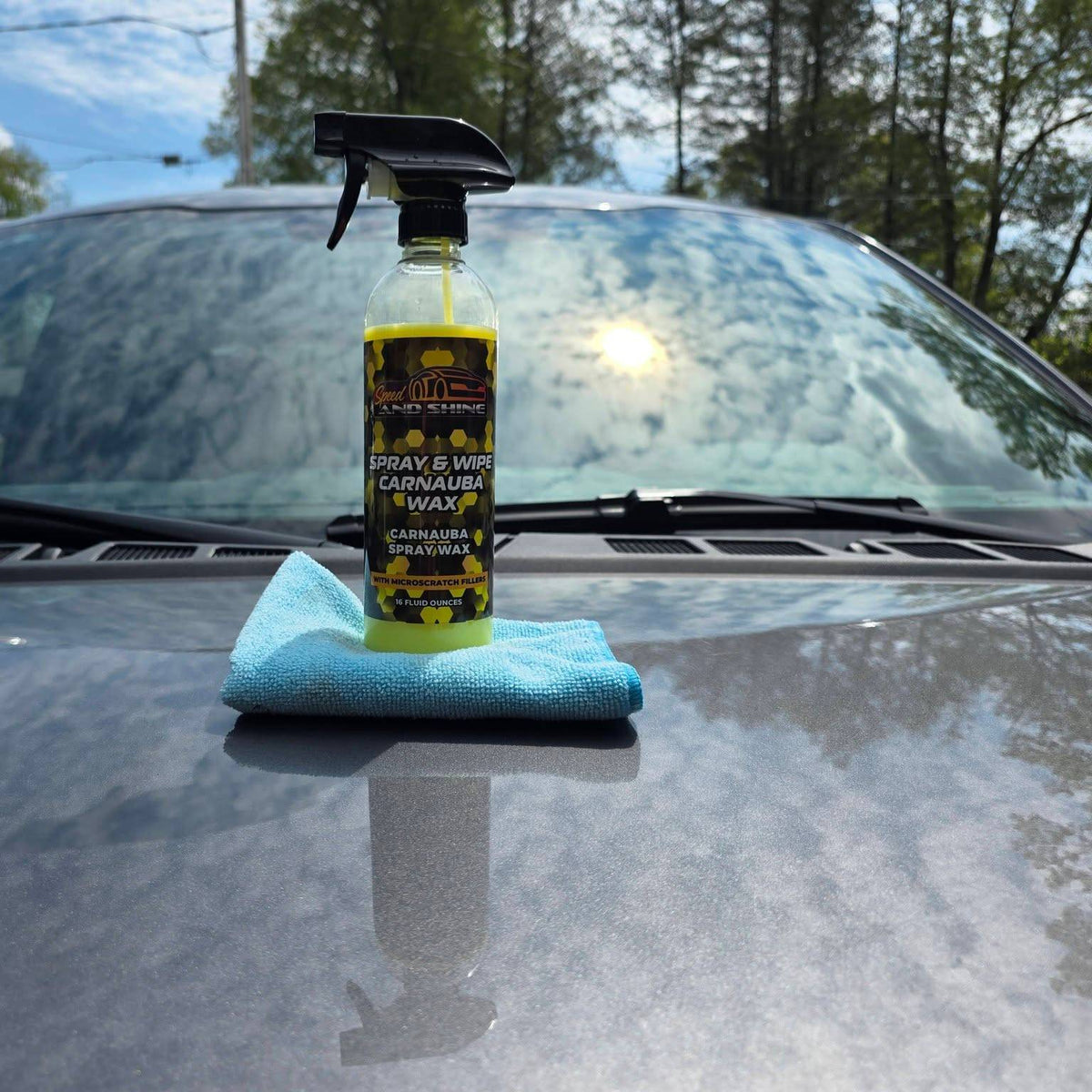 Spray & Wipe Carnauba Wax sits on a blue microfiber cloth on the hood of a gray car