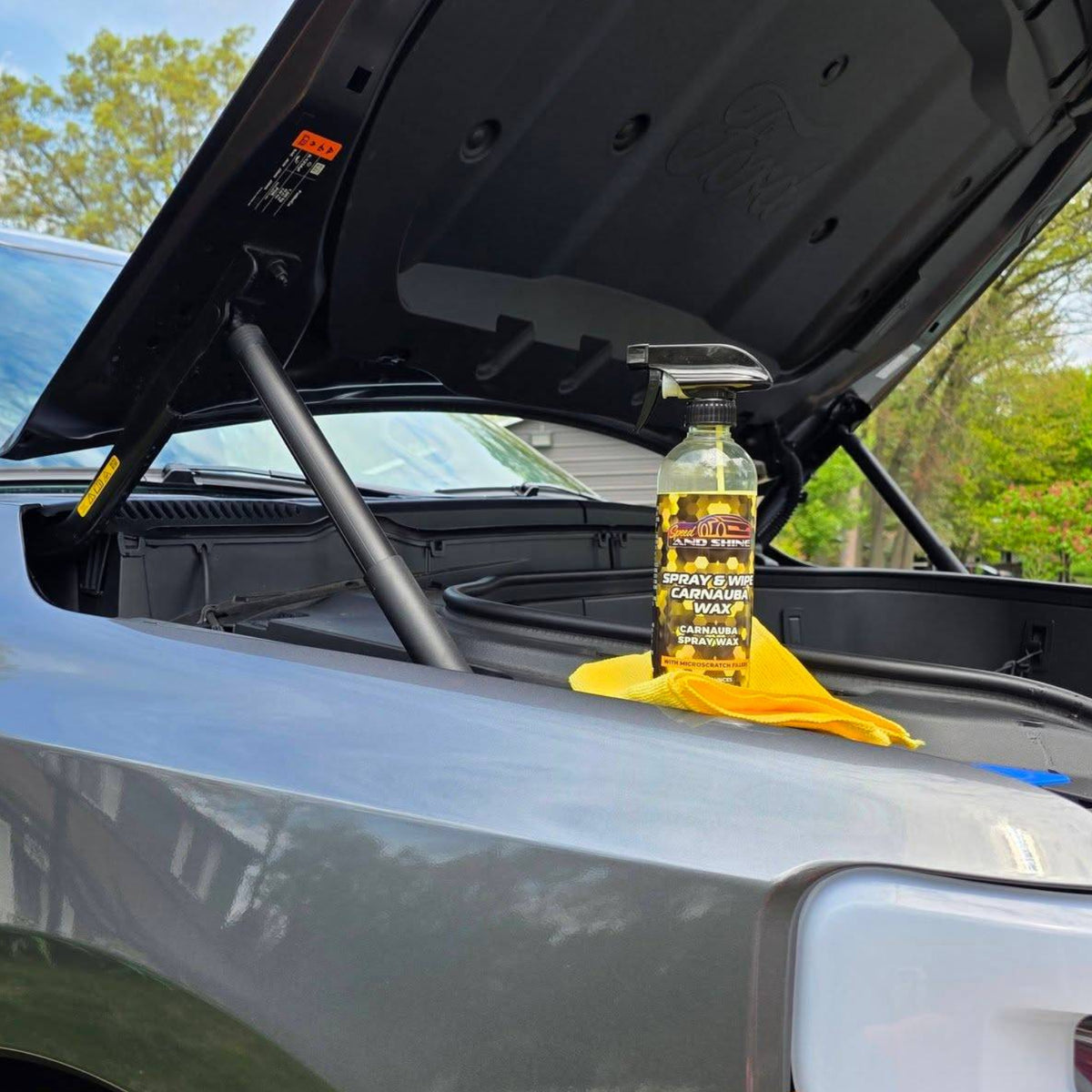 A bottle of Spray & Wipe Carnauba Wax resting on the open trunk of a silver car