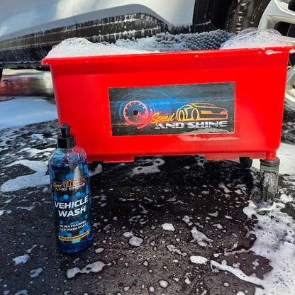 A red wash bin filled with soapy foam next to a bottle of Speed And Shine Vehicle Wash